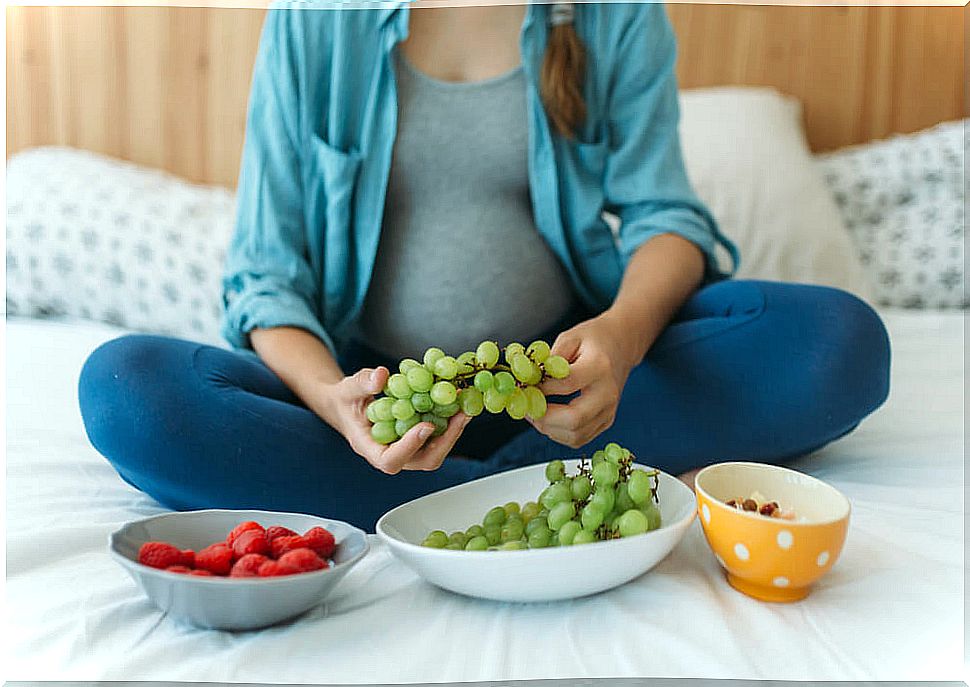 Pregnant woman eating grapes in bed.