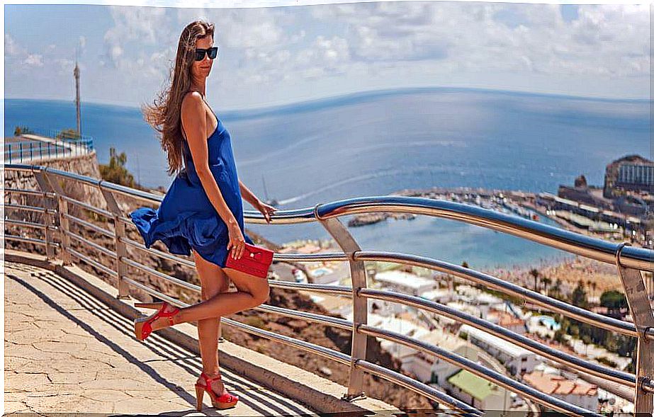 Girl poses in a blue dress and red high heels.